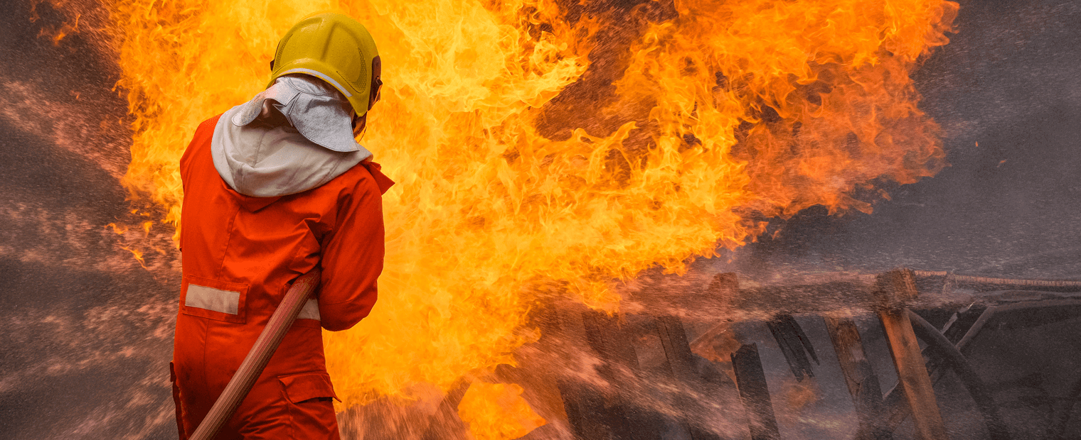 A fireman in protective gear aiming a hose at a fire.