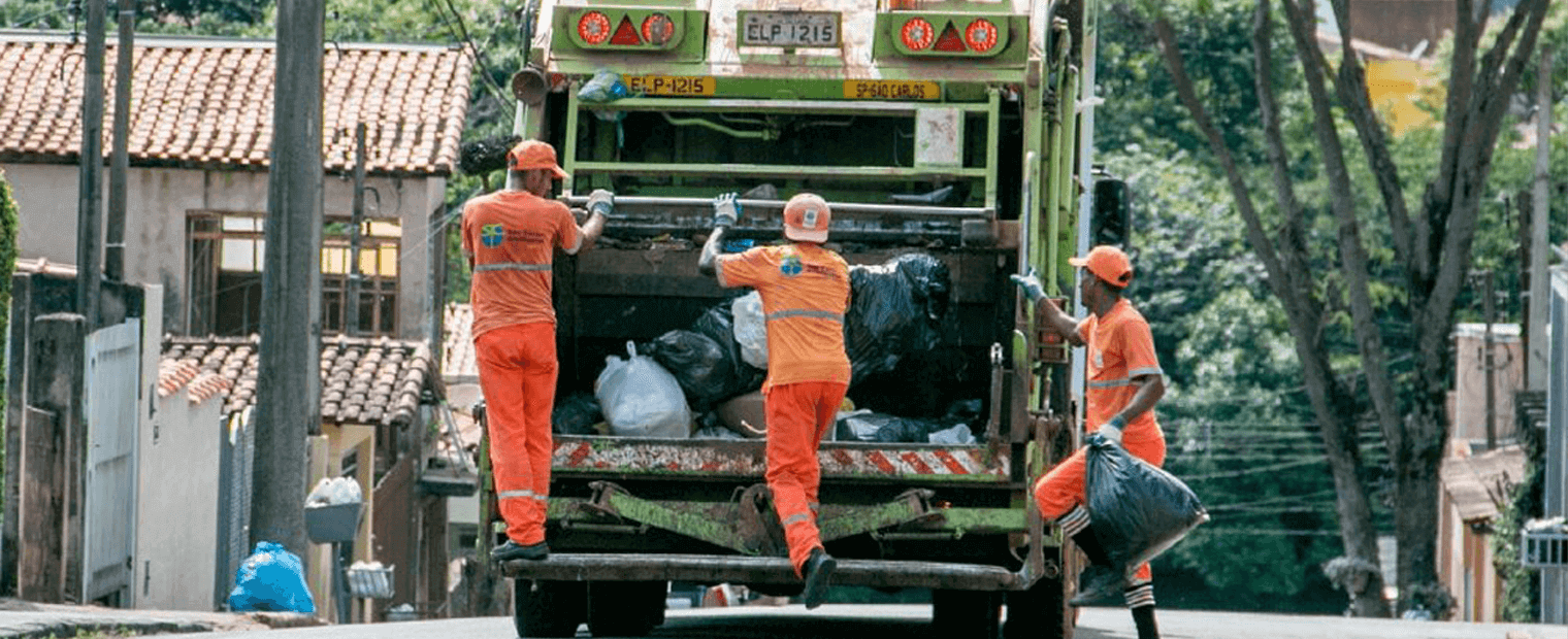 Three (3) waster collectors riding a waste collection truck.