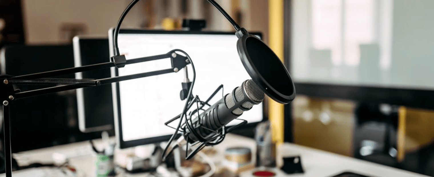 Microphone hanging from a boom arm and a pop-filter in front of a computer screen.