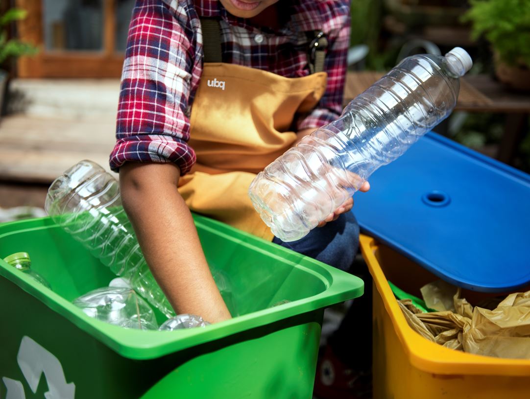 Person wearing a UBQ uniform sorting plastic bottles from a recycling bin.