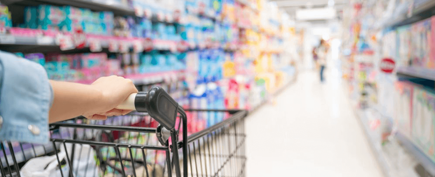 Woman pushing a supermarket cart through a supermarket alley filled with products.