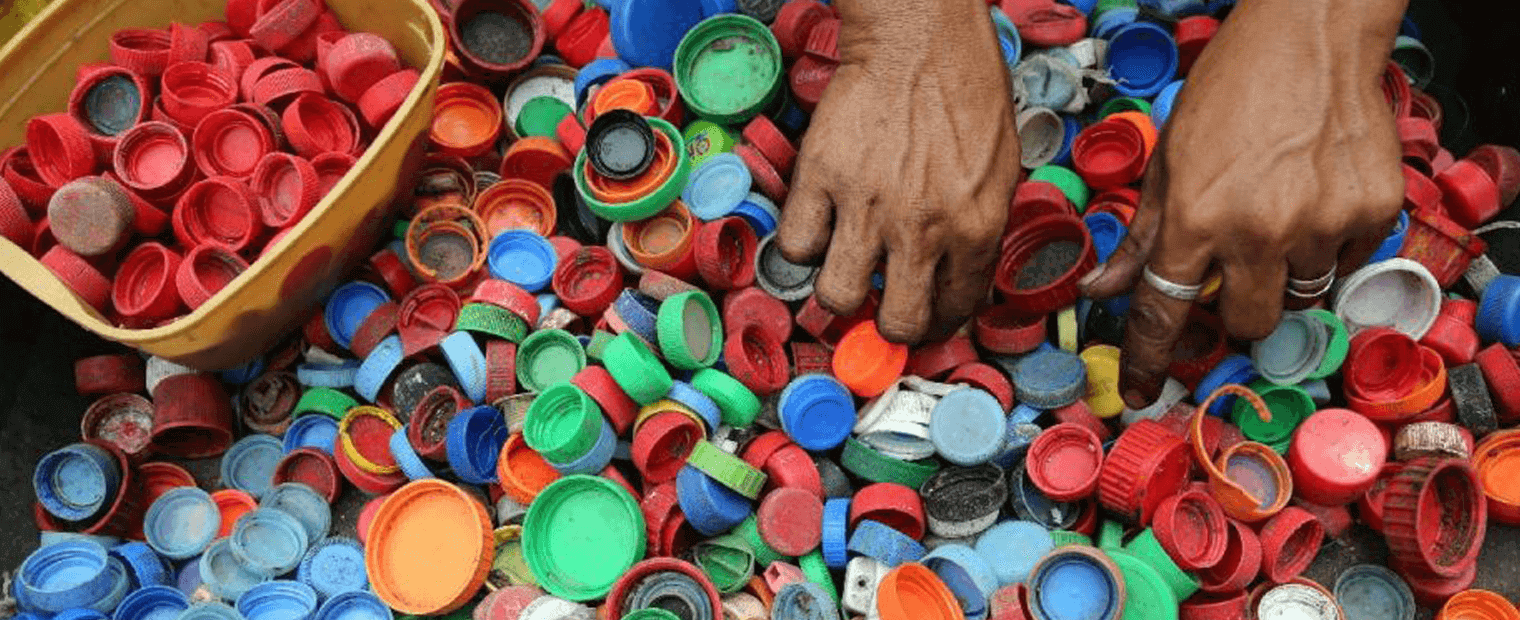 Hands sorting plastic bottle caps by color from a pile bottle caps.