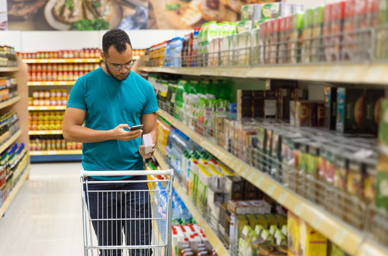 Man scanning a product label using his phone at a supermarket alley.