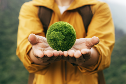 Man extending his arms holding a green ball made of grass.